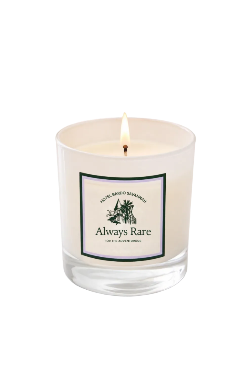A lit scented candle in a clear glass jar with a cream-colored wax and a white label that reads 'Always Rare' with a small illustration of a house and palm tree, set against a light gray background.