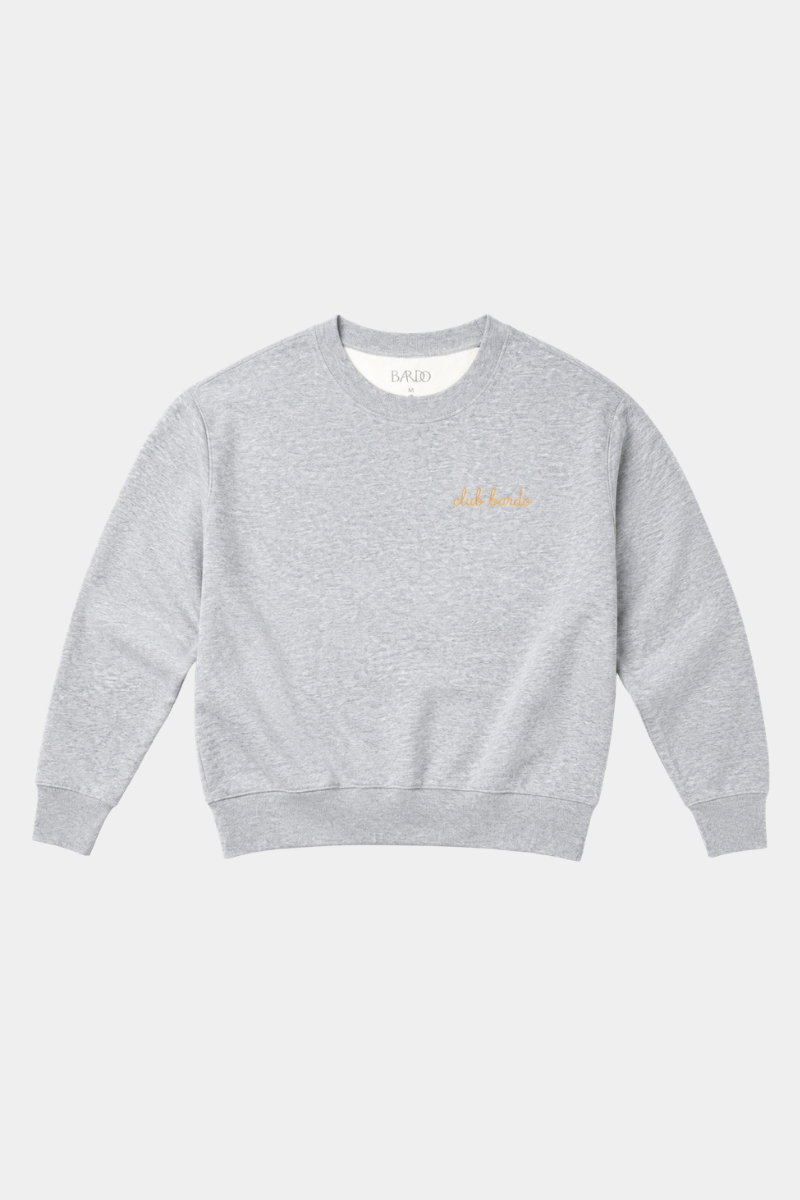 A light gray heather crewneck sweatshirt with a small gold embroidered script logo on the left chest, displayed flat against a light gray background.