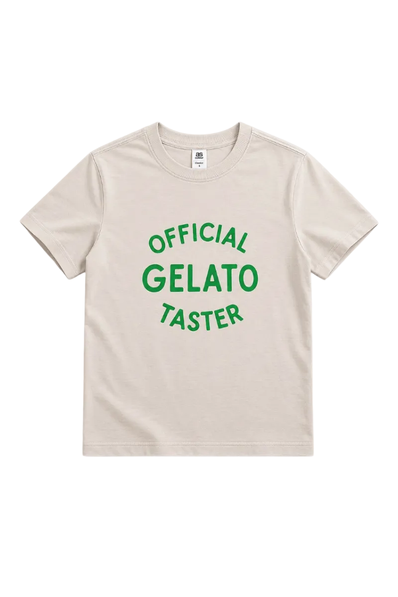A light beige crewneck t-shirt with green text reading 'OFFICIAL GELATO TASTER' printed on the front, displayed flat against a light gray background.