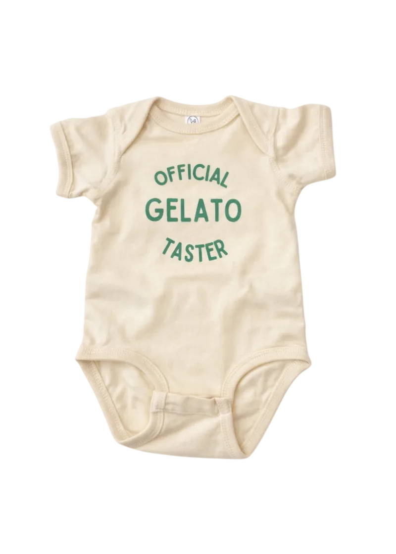 A short-sleeve baby bodysuit in cream with green text reading 'OFFICIAL GELATO TASTER' on the chest, shown flat against a white background.